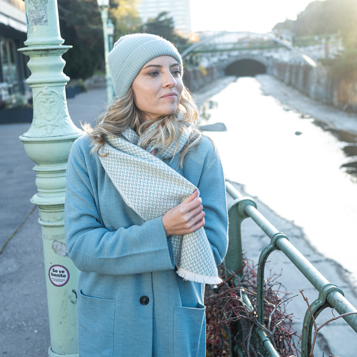 Woman wearing a cashmere herringbone narrow shawl by a river in winter, styled with a cozy hat.