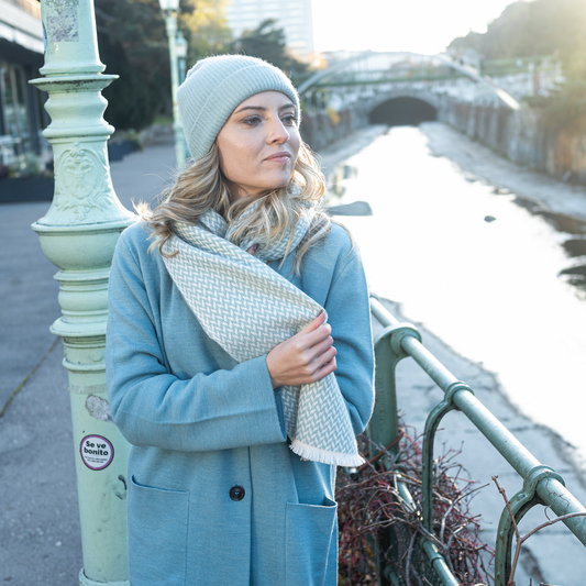 Woman wearing a cashmere herringbone narrow shawl by a river in winter, styled with a cozy hat.